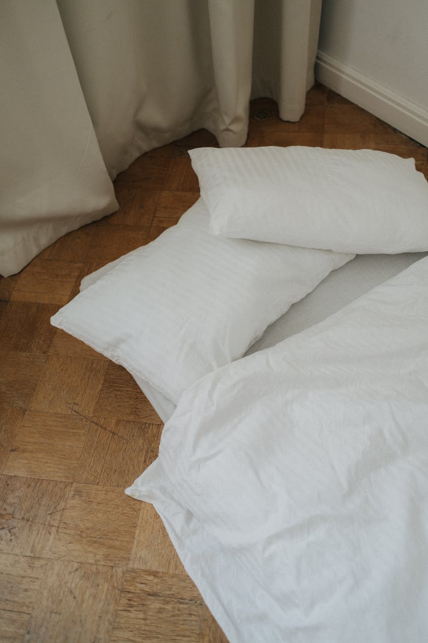 a bed with linens and pillows on the wooden floor