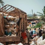 group of people in a garbage sorting plant next to bags of plastic bottles and a truck with waste paper