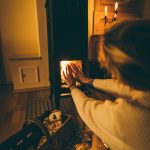 woman wearing white long sleeved try to get heat at fireplace