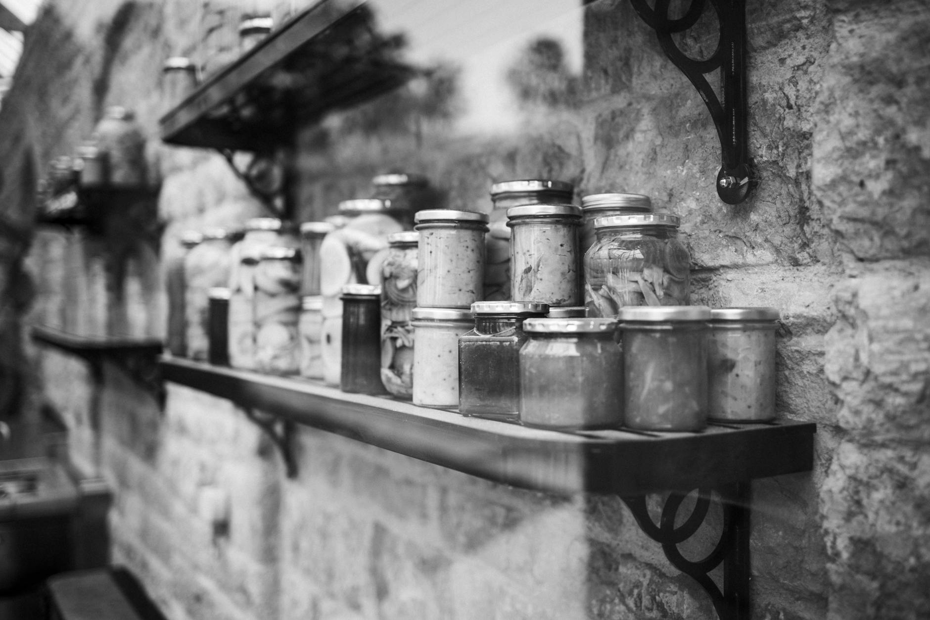 grayscale photography of glass jars on wooden shelf